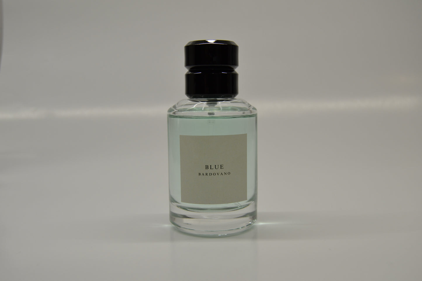 Clear bottle with black cap on a gray background and the name blue