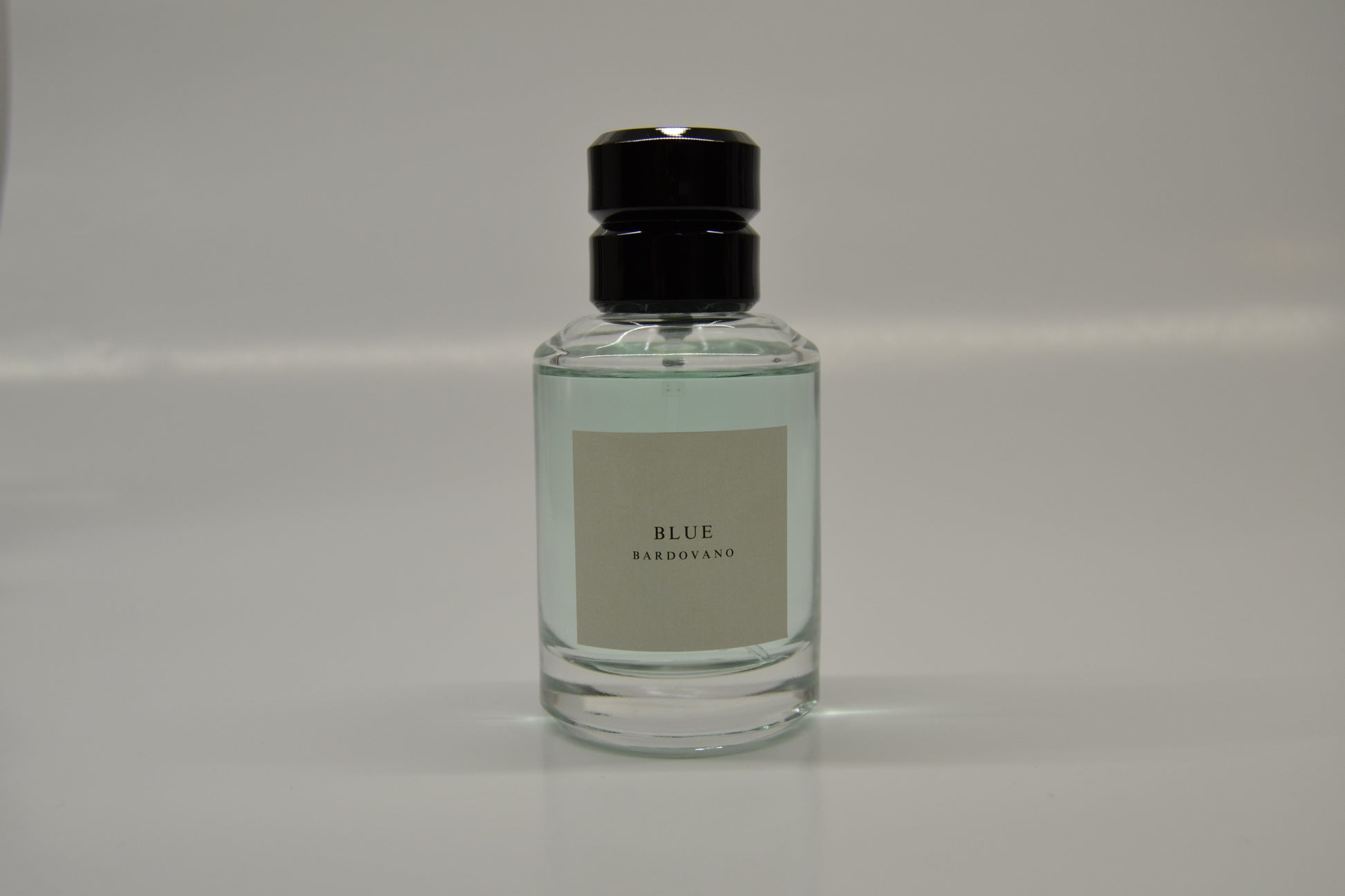 Clear bottle with black cap on a gray background and the name blue