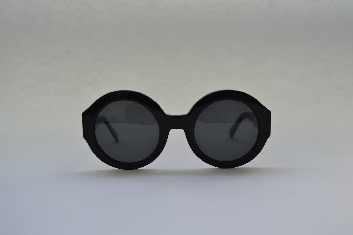 A pair of black, round-framed sunglasses with polarized lenses on a light background.